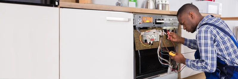 Appliance repair technician diagnosing a kitchen dishwasher with a multimeter. Appliance repair technician diagnosing a kitchen dishwasher with a multimeter.