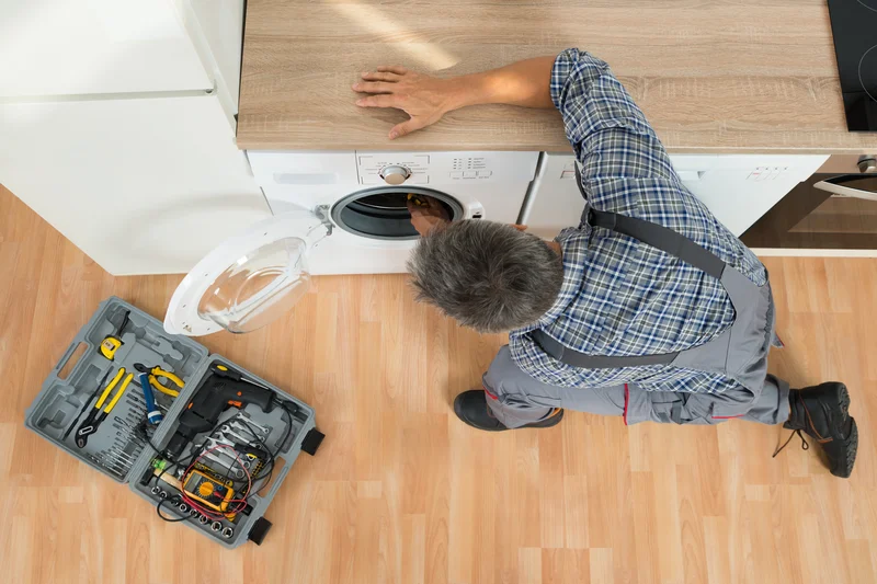 Overhead view of technician repairing a white front load washing machine with tools.