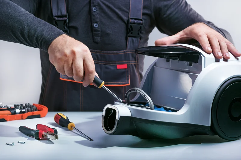 Technician repairing a canister vacuum cleaner at a work bench with tools Technician repairing a canister vacuum cleaner at a work bench with tools