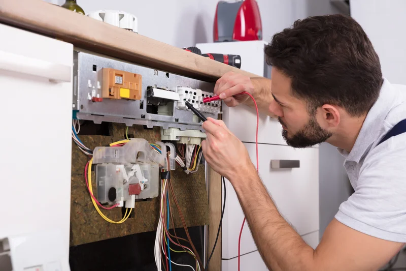 Technician testing a dishwasher control board using a digital multimeter.