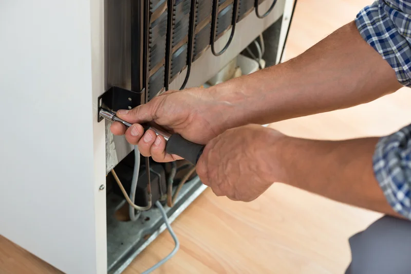 Close up of hands repairing refrigerator back panels with hand tool. Close up of hands repairing refrigerator back panels with hand tool.