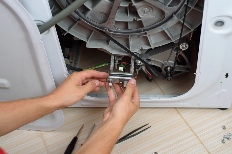 Appliance repairman fixing a broken washing machine heating element Appliance repairman fixing a broken washing machine heating element