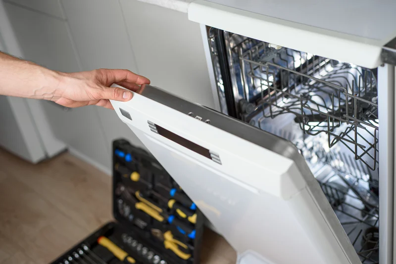 Professional repairman inspecting a kitchen dishwasher with tools Professional repairman inspecting a kitchen dishwasher with tools